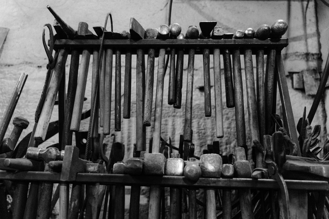 A monochrome display of various metal hammers arranged on a workshop rack.